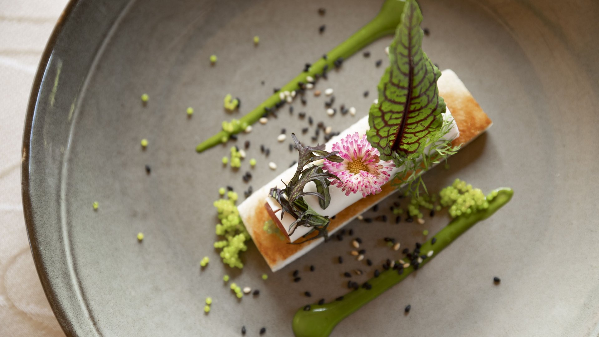 Il nostro hotel enogastronomico in Alto Adige: Burggräflerhof Piatto gourmet con crema, fiore commestibile, foglie e salsa verde nel piatto